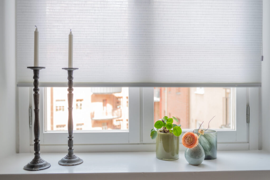 Vit plisségardin i fönster med ljusstakar på fönsterbänken